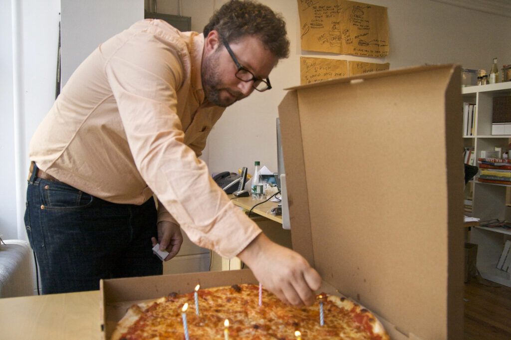 A man lights birthday candles on a pizza.